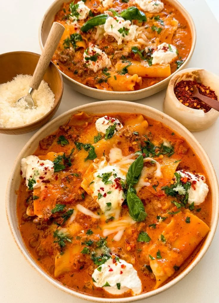 A warm bowl of lasagna soup topped with cheese and herbs