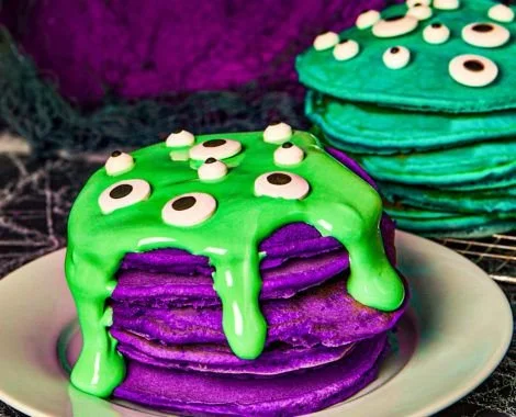 Stack of colorful Monster Pancakes topped with whipped cream and sprinkles