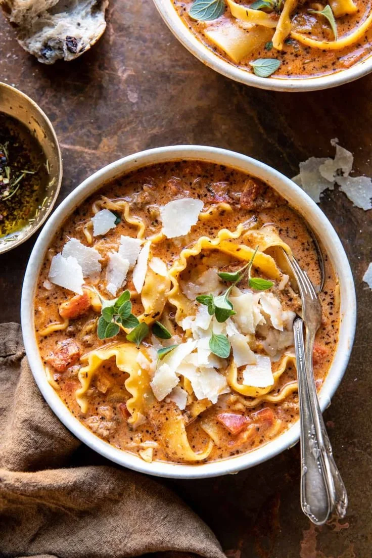 Bowl of spicy lasagna soup garnished with fresh basil and mozzarella cheese.
